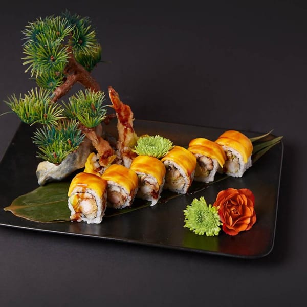 Raku's sushi platter with mango-topped rolls, tempura shrimp, and decorative bonsai, flowers, and leaves.