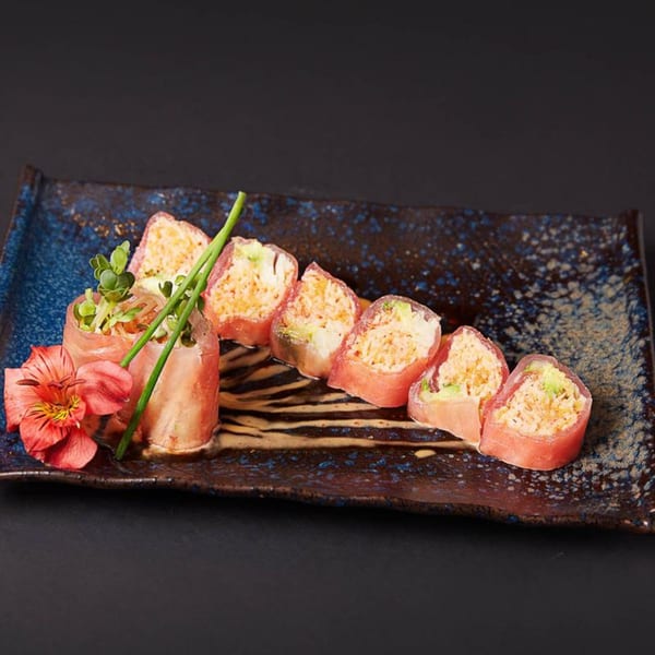 Raku's sushi rolls with pink tuna, avocado, and crab, garnished with chives and a red flower.