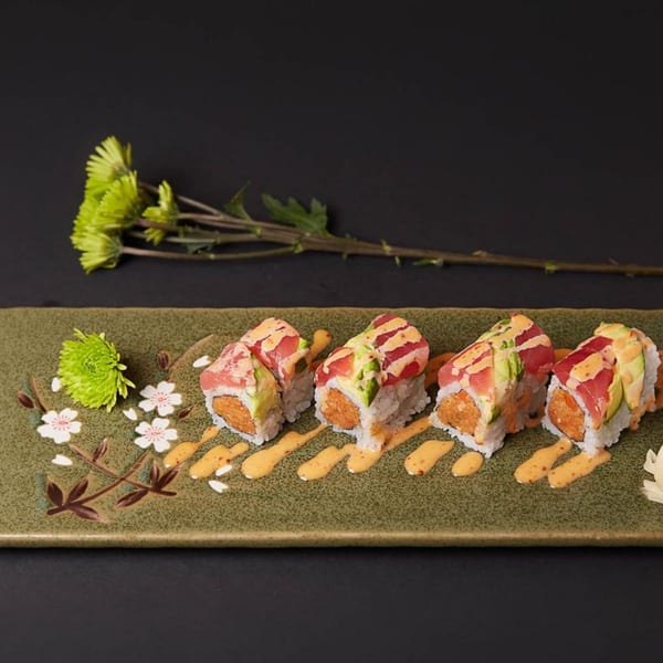 Raku sushi rolls with tuna, avocado, and spicy sauce on a decorative green plate with flowers.