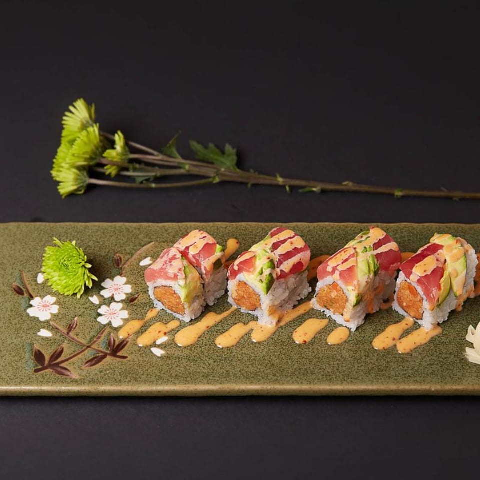 Raku sushi rolls with tuna, avocado, and spicy sauce on a decorative green plate with flowers.