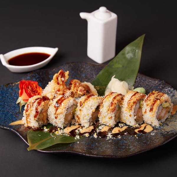 Raku sushi roll with crispy topping, drizzled sauce, and a side of soy sauce.
