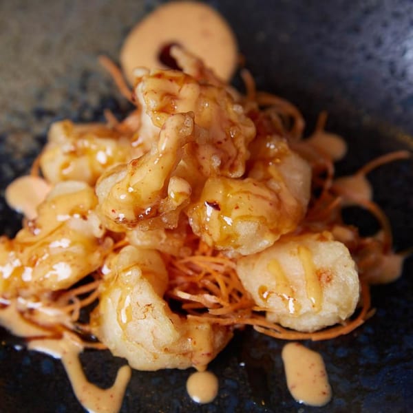 Crispy fried shrimp drizzled with a creamy orange sauce, served on a dark plate.