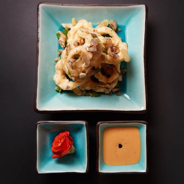 Crispy fried calamari rings on a blue plate, with a red flower and dipping sauce on the side.
