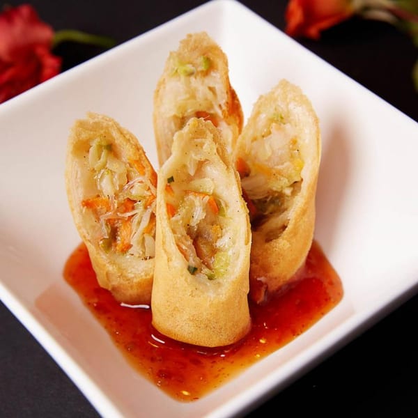 Four crispy spring rolls filled with vegetables, served with sweet chili sauce on a white plate.