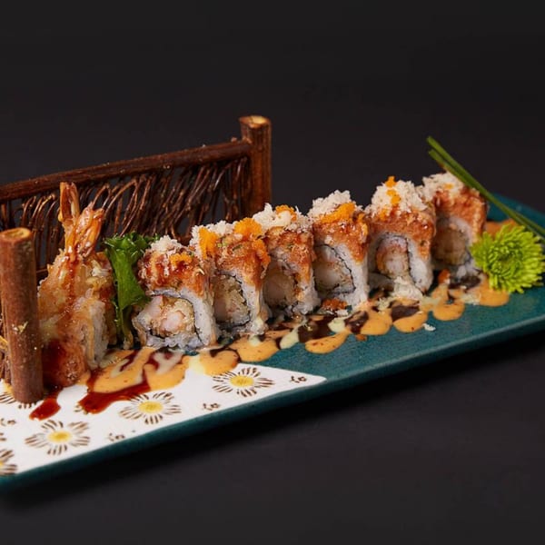 Raku's sushi roll with tempura shrimp, sauce, and orange roe, presented on a decorative plate.