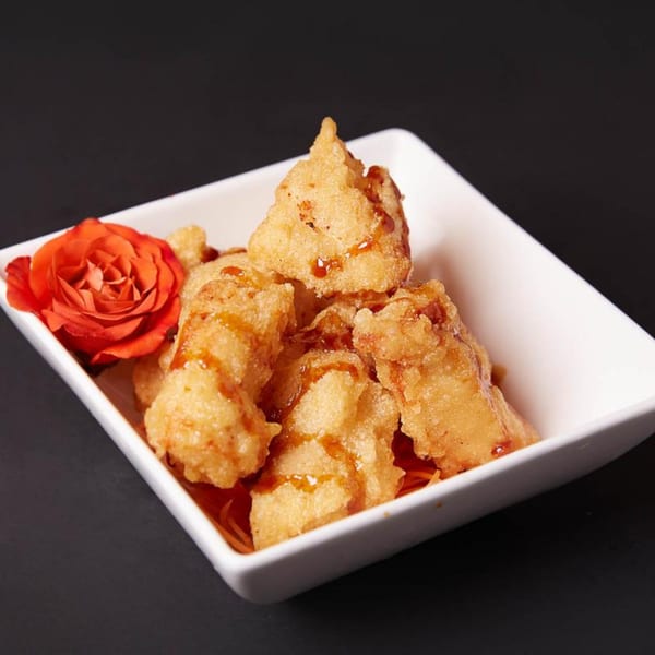 Crispy fried tempura pieces drizzled with sauce, garnished with a red rose in a white bowl.